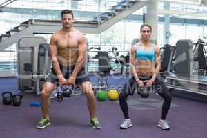 Bodybuilding man and woman lifting kettlebells in a squat