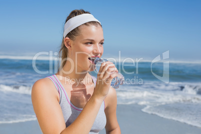 Sporty smiling blonde drinking water on the beach