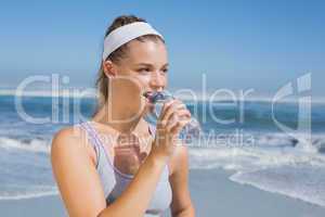 Sporty smiling blonde drinking water on the beach