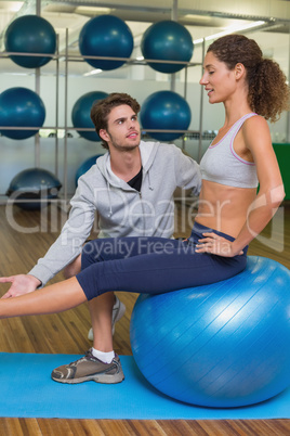 Trainer watching his client lift leg on exercise ball