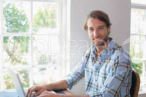 Smiling casual man using laptop looking at camera