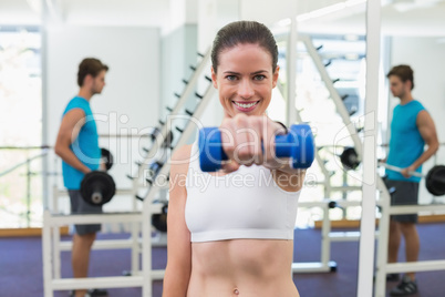 Fit brunette exercising with blue dumbbells