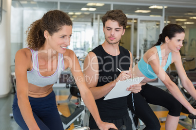 Fit women in a spin class with trainer taking notes