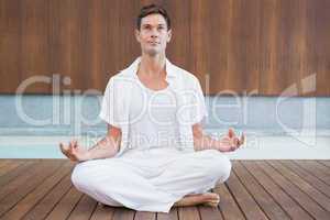 Handsome man in white meditating in lotus pose