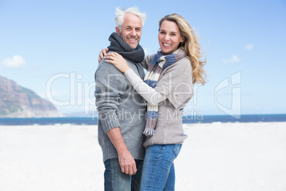 Smiling couple looking at camera on the beach in warm clothing