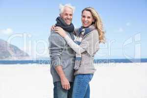 Smiling couple looking at camera on the beach in warm clothing