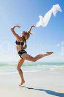 Fit blonde jumping gracefully with scarf on the beach