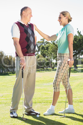 Golfing couple standing smiling at each other