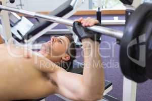 Shirtless bodybuilder lifting heavy barbell weight lying on benc