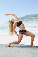 Fit blonde stretching her back on the beach