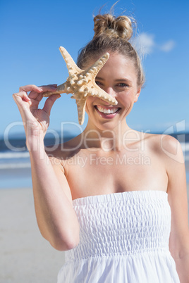 Pretty blonde in white dress holding starfish on the beach