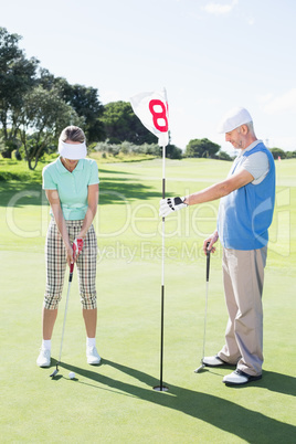 Golfer holding eighteenth hole flag for partner putting ball