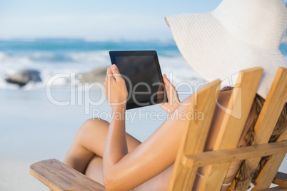 Woman in straw hat relaxing in deck chair on the beach using tab