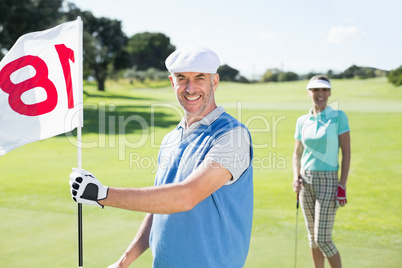 Happy golfer holding eighteenth hole flag with partner behind hi