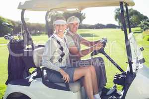 Happy golfing couple sitting in buggy smiling at camera