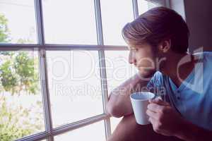 Thoughtful man sitting by the window having coffee