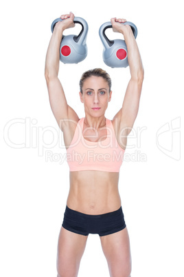 Serious female crossfitter lifting kettlebells above head