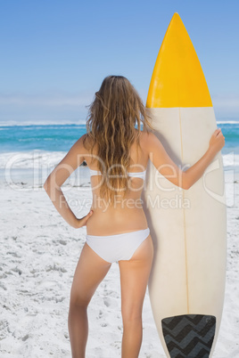 Fit surfer girl holding her surfboard on the beach