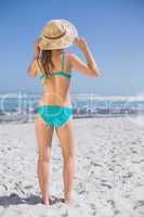 Slender woman in bikini on beach wearing sunhat
