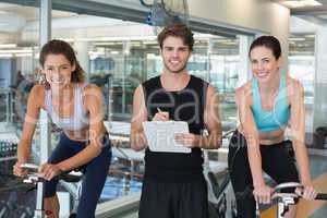 Fit women in a spin class with trainer smiling at camera