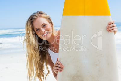 Blonde surfer holding her board smiling at camera