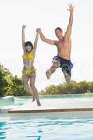 Excited couple jumping into swimming pool on holidays