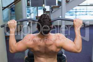 Shirtless bodybuilder using weight machine for arms