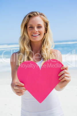 Smiling blonde showing pink heart on the beach