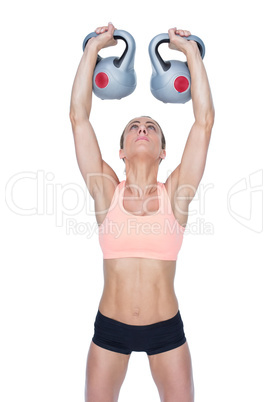 Serious female crossfitter lifting kettlebells above head