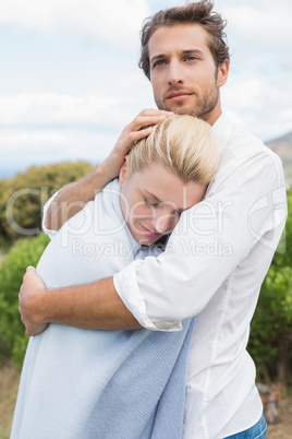 Protective man hugging his girlfriend in blue blanket outside