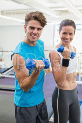 Fit couple exercising together with blue dumbbells