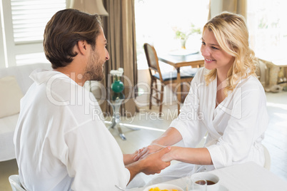 Cute couple in bathrobes having breakfast together holding hands