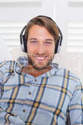 Casual smiling man lying on couch listening to music