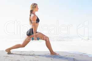Fit blonde doing weighted lunges on the beach