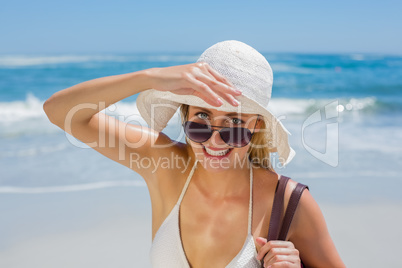 Smiling blonde in white bikini carrying bag on the beach