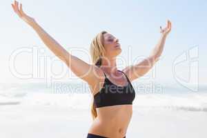 Fit blonde standing on the beach with arms outstretched