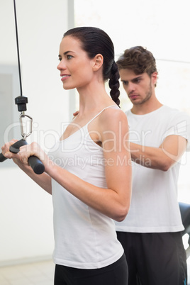 Fit smiling woman using weights machine for arms with her traine