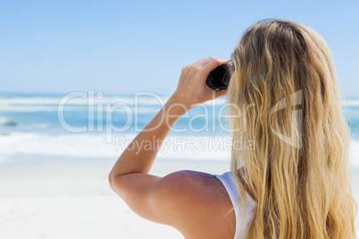 Blonde looking to the ocean through binoculars