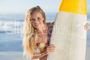 Gorgeous blonde surfer in bikini holding her board