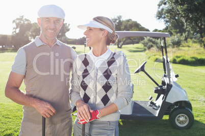 Happy golfing couple with golf buggy behind