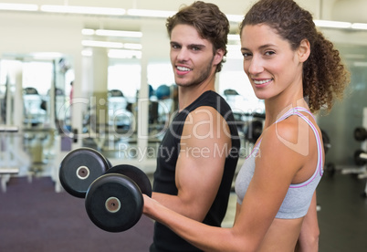 Fit couple lifting dumbbells together smiling at camera