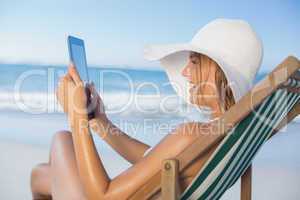 Smiling woman relaxing in deck chair on the beach using tablet