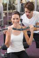 Fit brunette using weights machine for arms with trainer helping