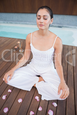 Peaceful brunette in white sitting in lotus pose surrounded by p
