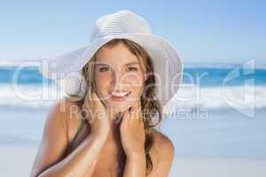 Beautiful girl in white straw hat smiling at camera on beach