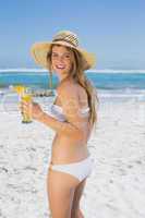 Pretty smiling blonde in bikini sipping cocktail on the beach
