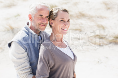 Happy hugging couple on the beach looking away