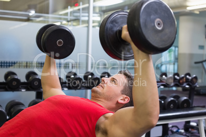 Bodybuilder lying on bench lifting dumbbells