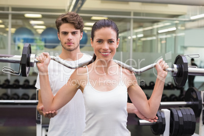 Fit smiling woman lifting barbell with her trainer