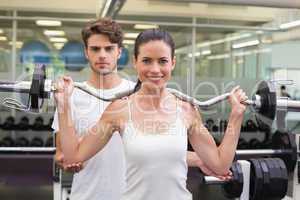 Fit smiling woman lifting barbell with her trainer